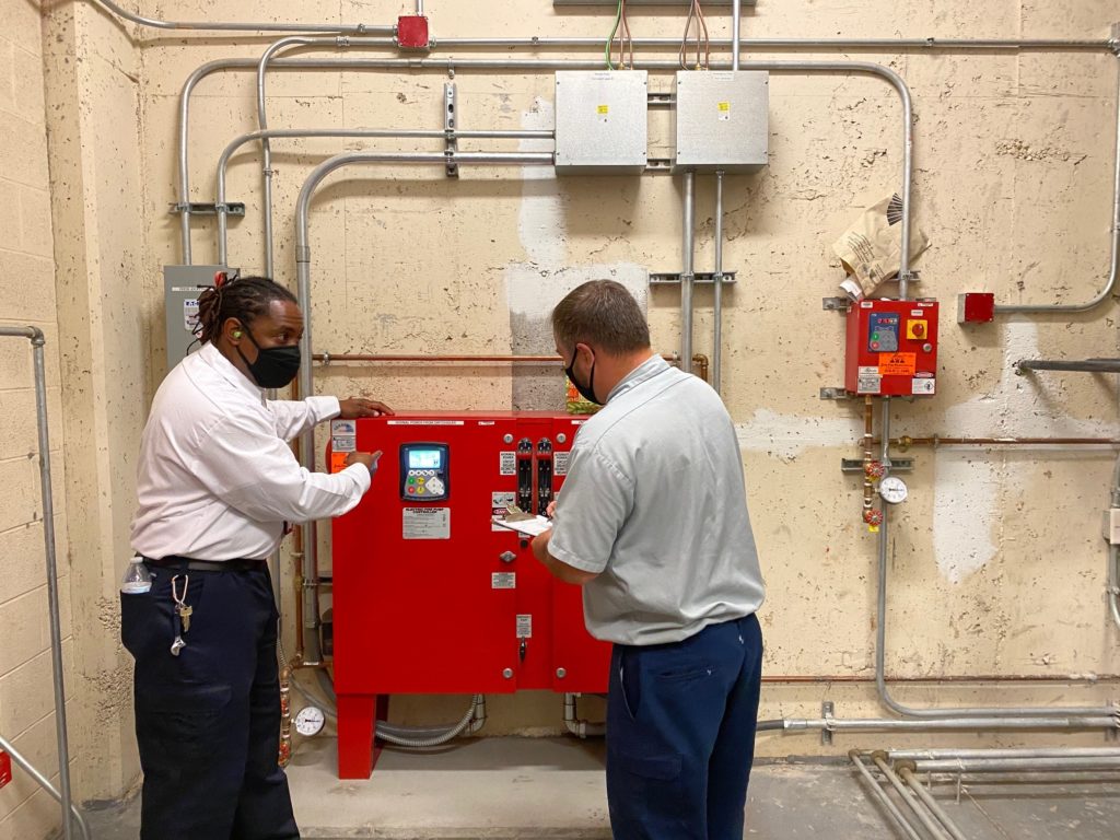 two men in white shirts are working on a red machine